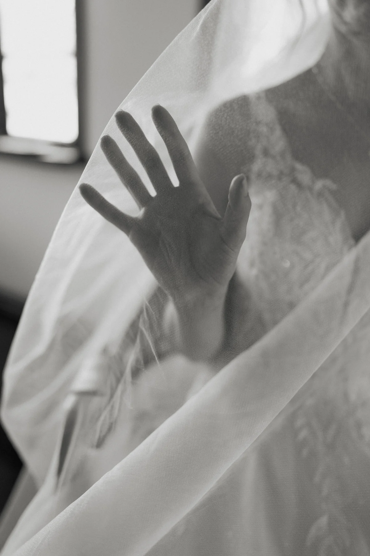 A hand beneath a translucent bridal veil, photographed in black and white